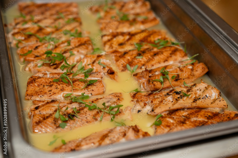 Salmon in garlic sauce in a metal catering dish being served at an event Salmon in garlic sauce in a metal catering dish being served at an event