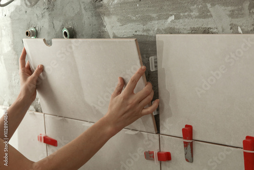 Woman tiling bathroom walls, applying adhesive on a tile and placing ceramic tile in right position. Process of installation of tiles in the bathroom step by step. DIY home improvement.	 photo