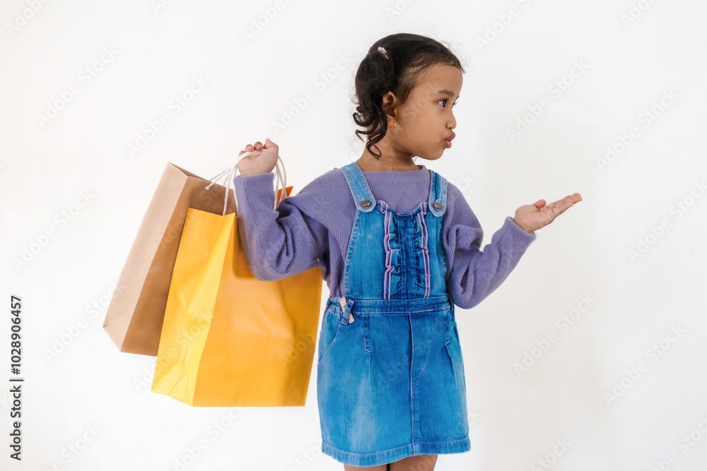 Excited little Asian girl looking and pointing at something to the side while holding paper shopping bags Excited little Asian girl looking and pointing at something to the side while holding paper shopping bags