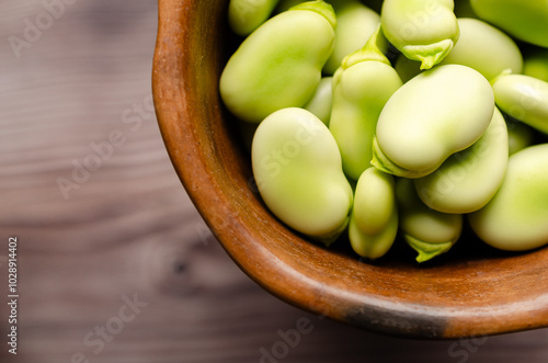 Fresh fava beans in a clay bowl on a wooden background. 