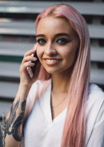 Close up portrait of positive female teenager with pink hair enjoying good internet connection on cellphone, happy woman with tattoo smiling at camera while phoning to best friend via smartphone app