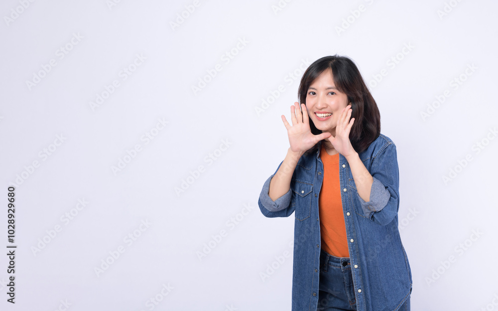 An Asian woman wearing orange t shirt and denim jean is posing with a shouting gesture against a white background. An Asian woman wearing orange t shirt and denim jean is posing with a shouting gesture against a white background.