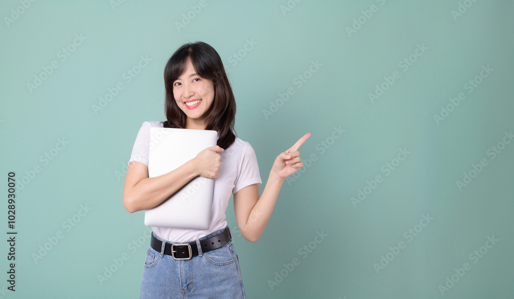 Technology lover. Cheerful asian woman hugging laptop while pointing finger to free empty copy space. Casual female hug laptop isolated on green background. Back to school concept for advertisement. Technology lover. Cheerful asian woman hugging laptop while pointing finger to free empty copy space. Casual female hug laptop isolated on green background. Back to school concept for advertisement.