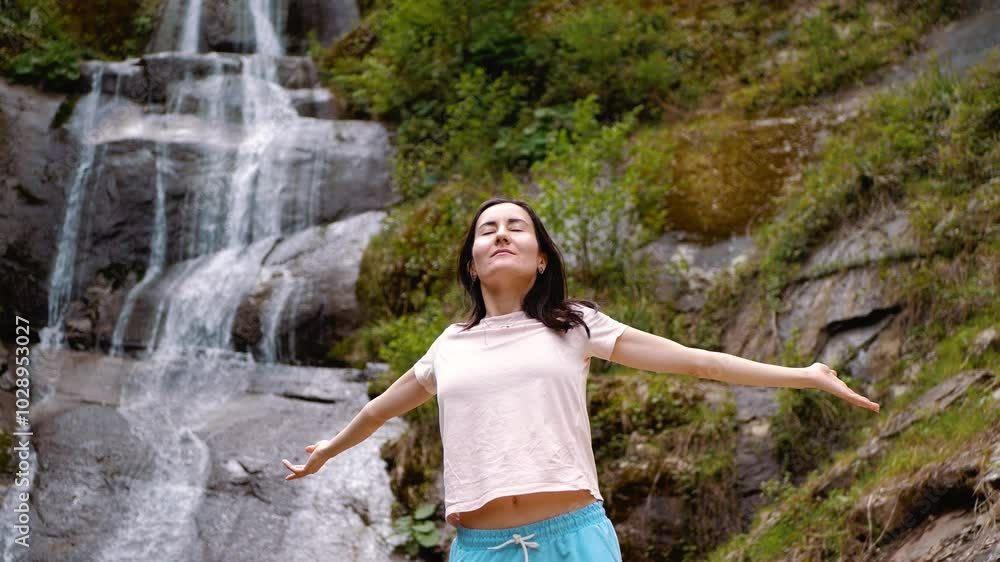 A girl against the backdrop of a waterfall spreads her arms. Joy of life and success. Achieving goals and results A girl against the backdrop of a waterfall spreads her arms. Joy of life and success. Achieving goals and results