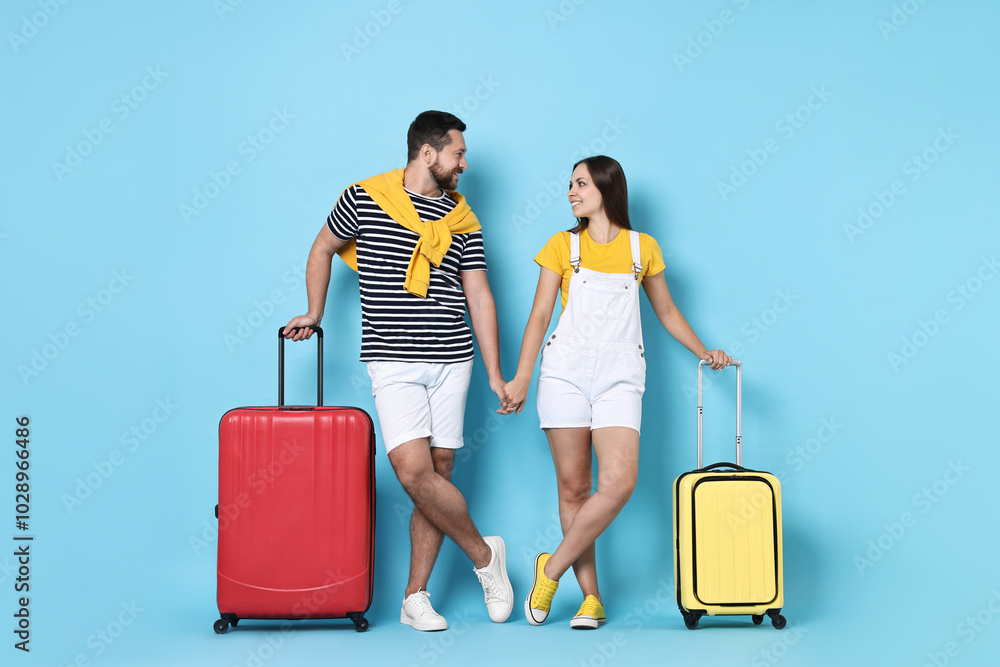 Happy couple with suitcases on light blue background Happy couple with suitcases on light blue background
