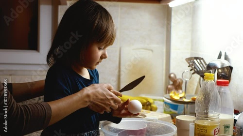Mom and little daughter cook together. Breaks an egg