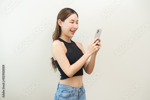 Happy asian young woman using mobile smart phone, read good news online, laugh excited getting offer, great positive surprise, celebrate success on smartphone. Smile girl isolated on white background. photo