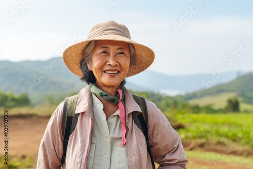 Portrait of a tender asian woman in her 70s sporting a breathable hiking shirt over backdrop of an idyllic countryside photo