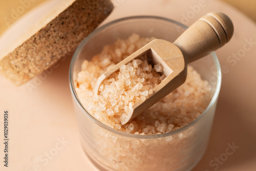 Close view of sea salt for relax bath in glass jare and wooden spoon on beige background. photo