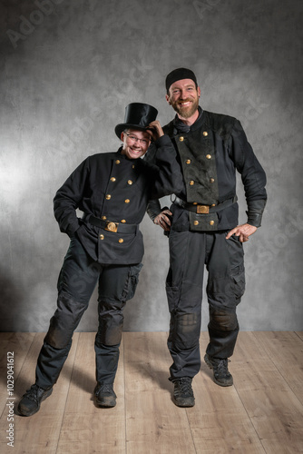 Schornsteinfegerin und Schornsteinfeger in Arbeitskleidung, gut gelaunt im Studio.