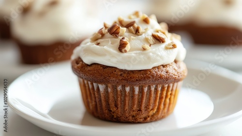 Close-up of a fluffy vegan carrot muffin garnished with chopped nuts and creamy frosting on a pristine white plate, perfect for a healthy dessert concept.