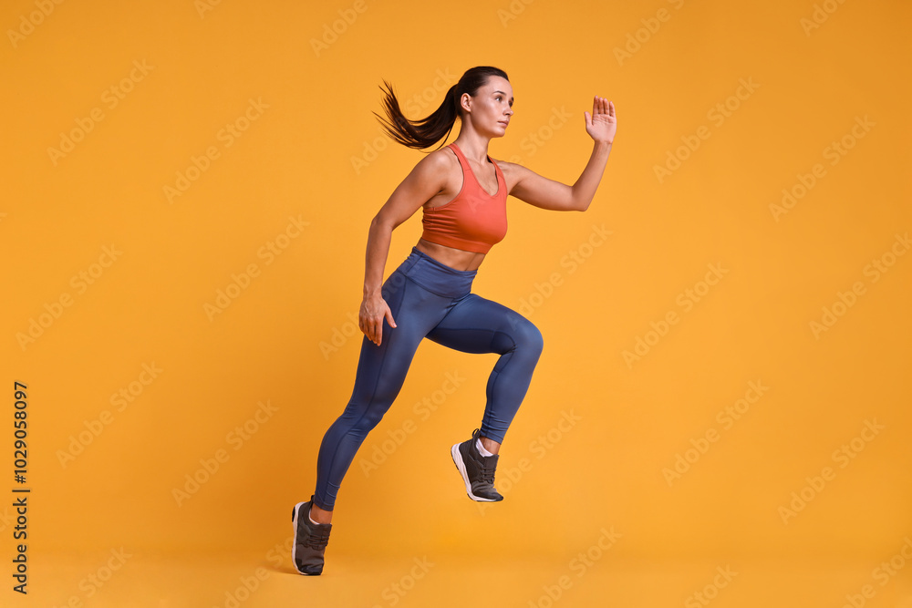 Woman in sportswear running on orange background Woman in sportswear running on orange background