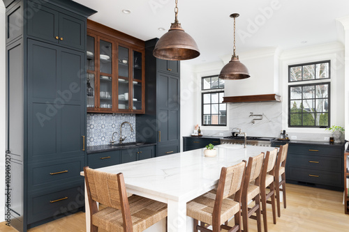 A modern farmhouse kitchen with blue and wood cabinets, brushed bronze pendant lights hanging over a large white island, and a blue and white tiled backsplash. No brands or labels.