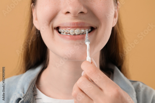 Wallpaper Mural Girl with braces cleaning teeth with interdental brush on beige background, closeup Torontodigital.ca