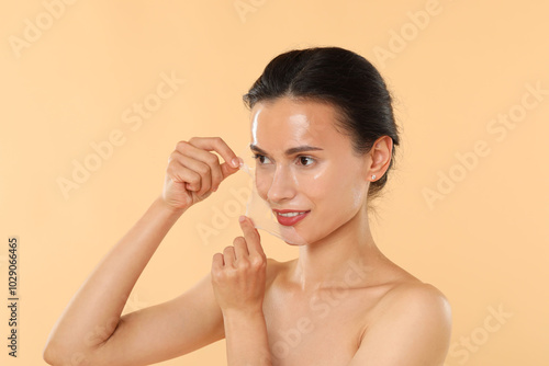 Smiling woman peeling off face mask on beige background photo