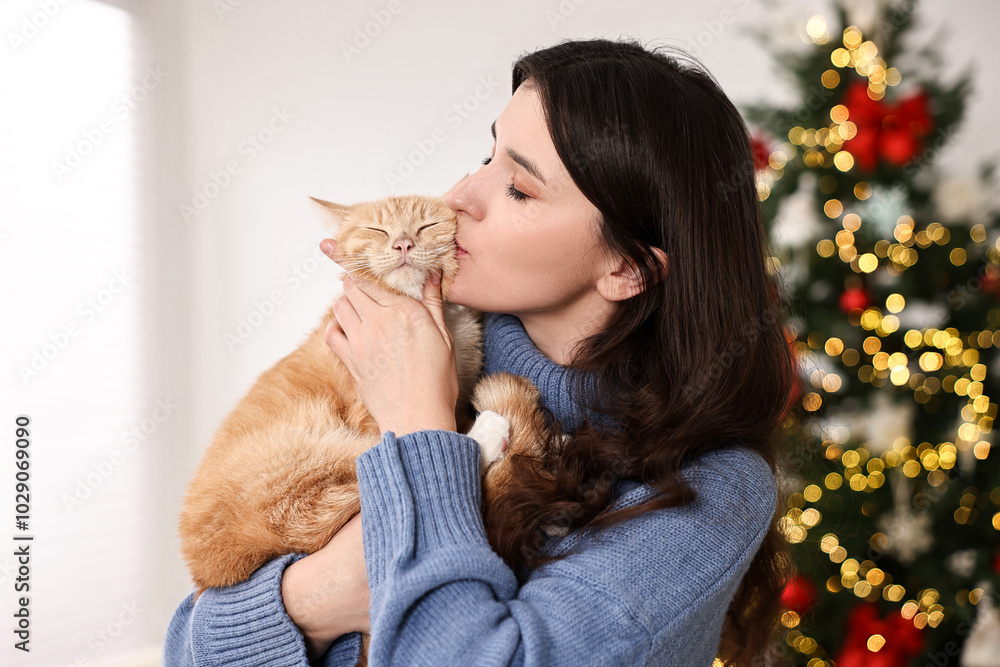 Woman kissing her cute ginger cat in room decorated for Christmas Woman kissing her cute ginger cat in room decorated for Christmas