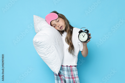 Overslept girl with sleep mask, pillow and alarm clock on light blue background