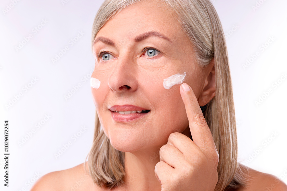 Senior woman applying face cream on white background Senior woman applying face cream on white background