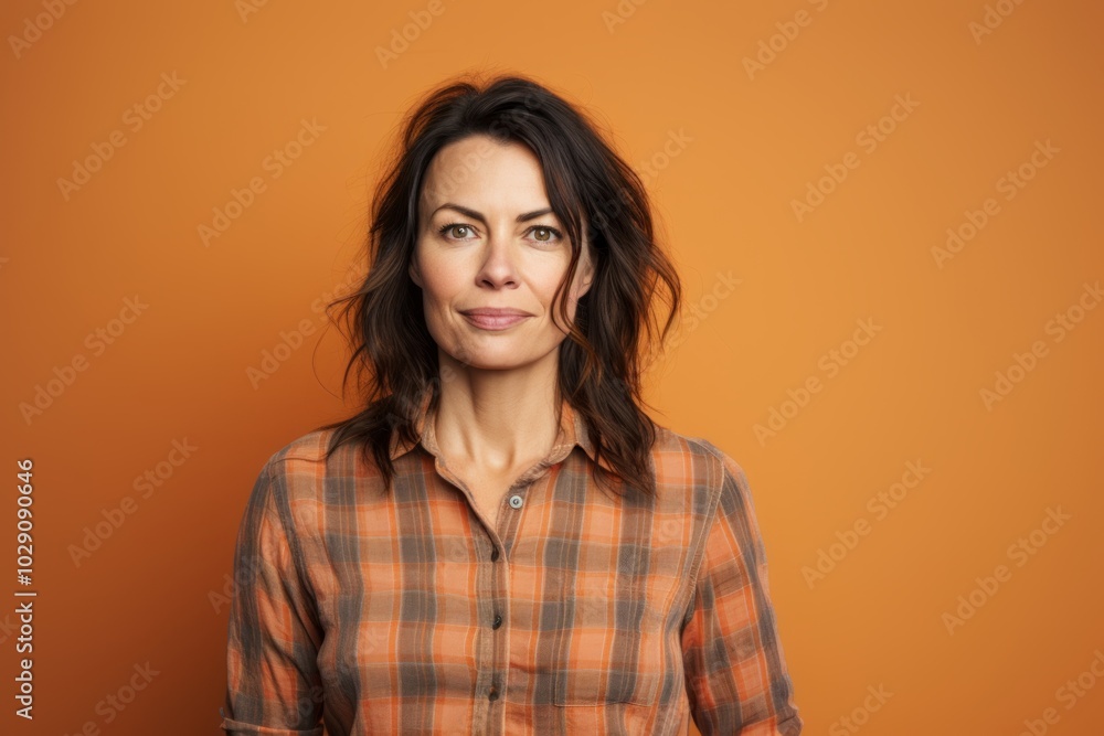 Portrait of a glad woman in her 40s dressed in a relaxed flannel shirt in pastel orange background Portrait of a glad woman in her 40s dressed in a relaxed flannel shirt in pastel orange background