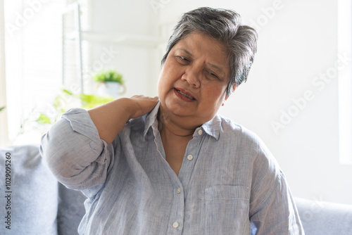 Pain body muscles stiff problem, suffer asian senior woman painful, older hand holding neck ache and aged holding massaging rubbing body, injury hurt,sore sitting on sofa at home. Health care concept.