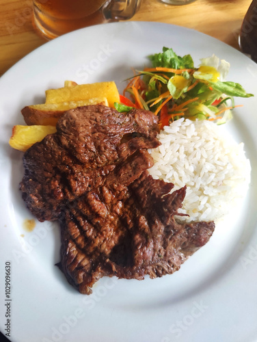 Plato de carne de alphaca asada acompañado de arroz, papas fritas y ensalada fresca, servido en un ambiente acogedor.