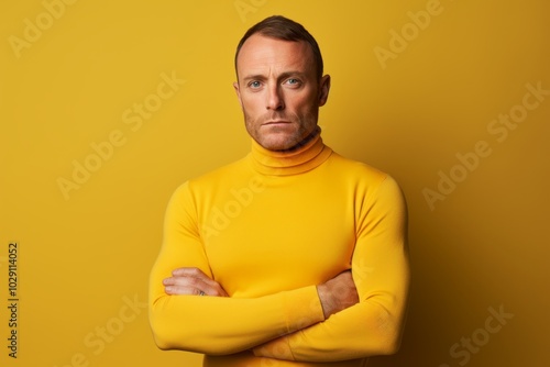 Portrait of a content man in his 40s wearing a classic turtleneck sweater in front of soft yellow background