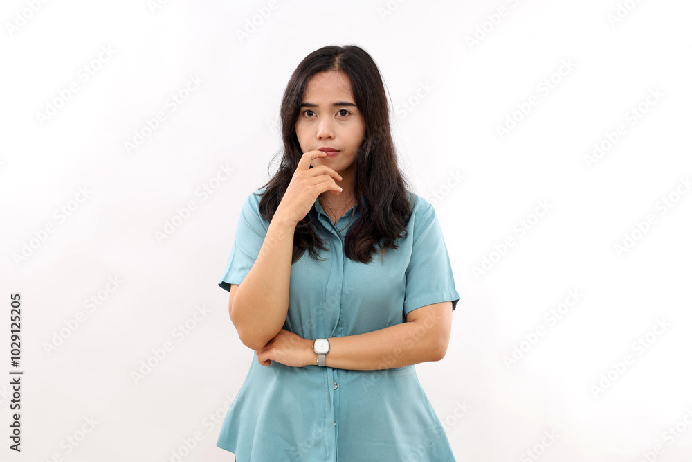 Photo of confused Asian girl bites lips and looks nervous at camera, holds hands partly crossed, dressed in casual shirt, stands against white wall with blank space aside Photo of confused Asian girl bites lips and looks nervous at camera, holds hands partly crossed, dressed in casual shirt, stands against white wall with blank space aside
