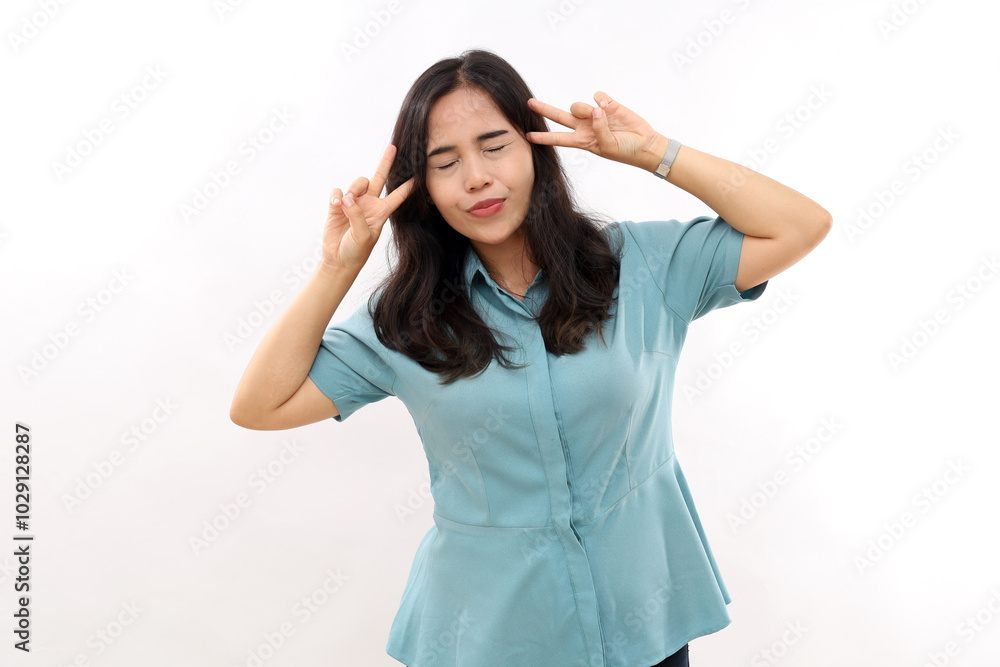 Fashionable lovely young woman has dark hair, closes eyes, makes peace gesture, gives victory sign, wears stylish outfit, poses against white background, isolated. People, body language concept Fashionable lovely young woman has dark hair, closes eyes, makes peace gesture, gives victory sign, wears stylish outfit, poses against white background, isolated. People, body language concept
