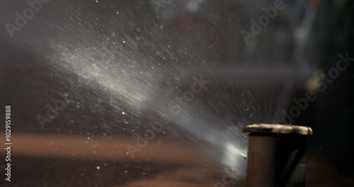 Tennis court sprinkler emitting a powerful water spray, captured in slow-motion, droplets scattering in various directions, showing dynamic movement photo