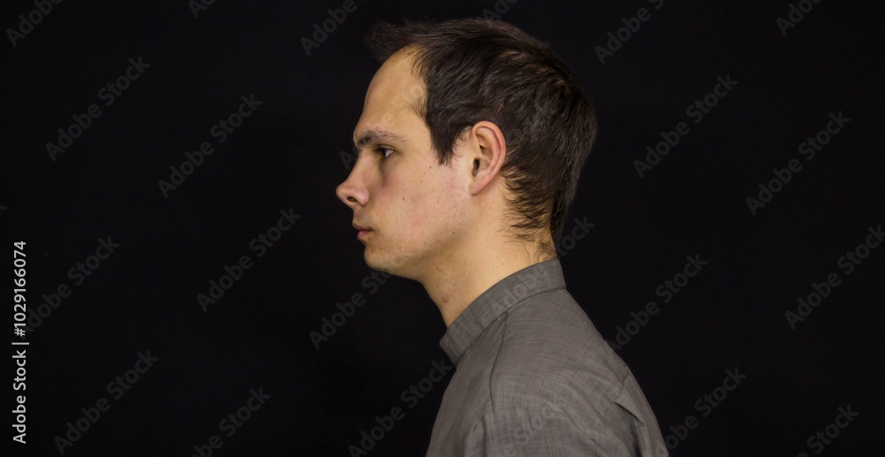 A guy with dark hair in a gray shirt stands in profile on a black background
A guy with dark hair in a gray shirt stands in profile on a black background