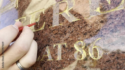 Renovation of golden letters text on a grave with some gold paint and brush