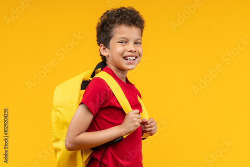 Studio portrait of happy smiling African American kid student posing over bright colored orange yellow background