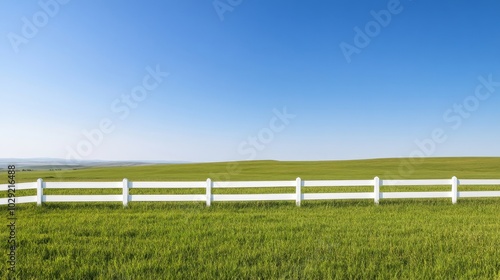 A white fence winds through the green countryside under a clear blue sky.