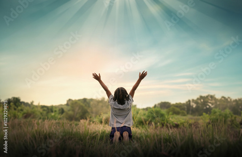 Praising the lord concept. Back view of a young girl with her arms raised to the sky in thankfulness and prayer. Themes such as Spirit, Glory, Blessing, Surrender, Trust, Peace, Joy photo