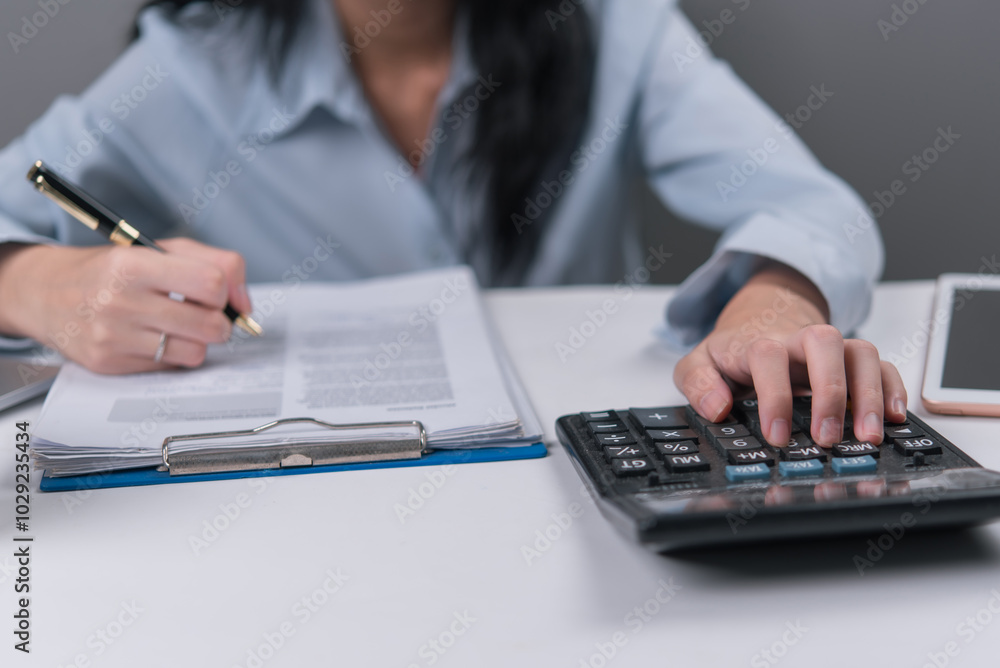 Woman using a calculator and writing on documents, symbolizing financial planning or business accounting. Woman using a calculator and writing on documents, symbolizing financial planning or business accounting.