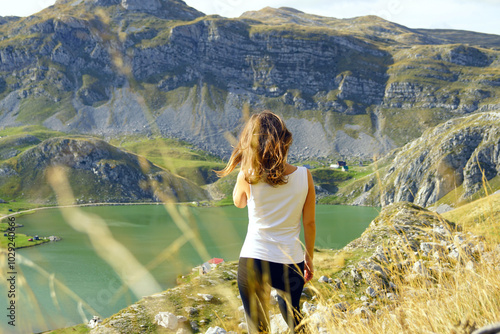 A girl photographed from the back stands in the mountains and looks at a beautiful landscape with a lake. Outdoor recreation: a female tourist walking above Kapetanovo Lake near Niksic, Montenegro. photo