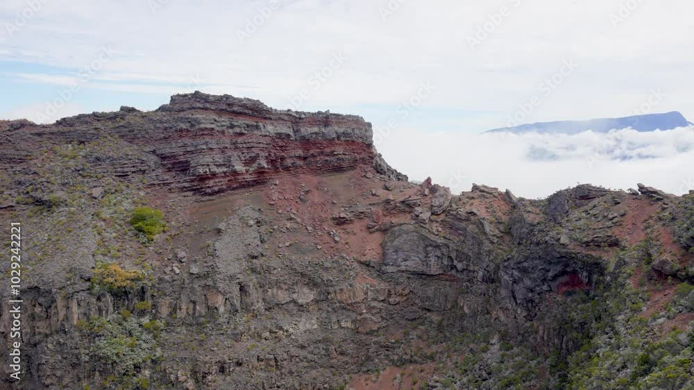 A close-up view of a volcanic crater on Piton de la Fournaise, Reunion Island. The steep, rugged walls of the crater are covered in lush vegetation, contrasting with the barren, rocky interior. A close-up view of a volcanic crater on Piton de la Fournaise, Reunion Island. The steep, rugged walls of the crater are covered in lush vegetation, contrasting with the barren, rocky interior.