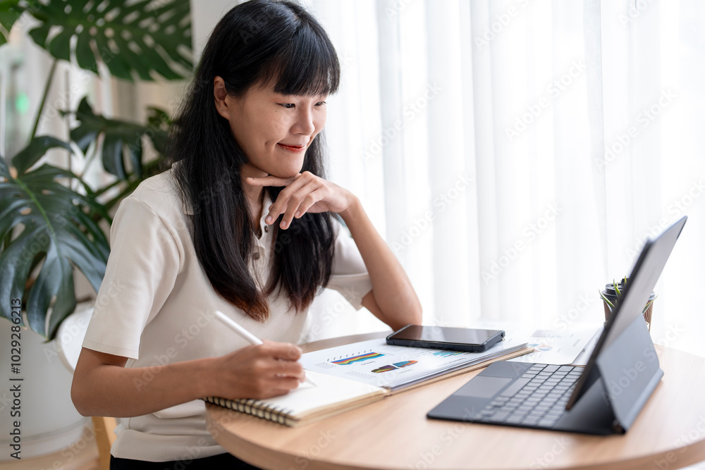 Asian businesswoman taking notes while looking at tablet screen Asian businesswoman taking notes while looking at tablet screen