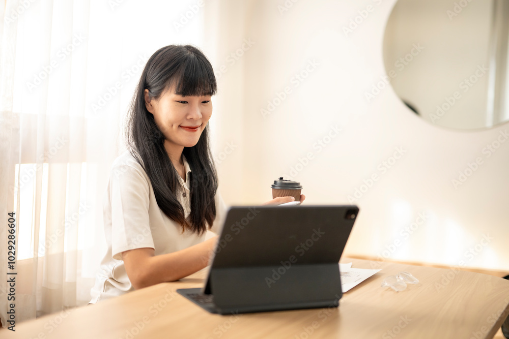 Young asian woman working from home using digital tablet and drinking coffee Young asian woman working from home using digital tablet and drinking coffee