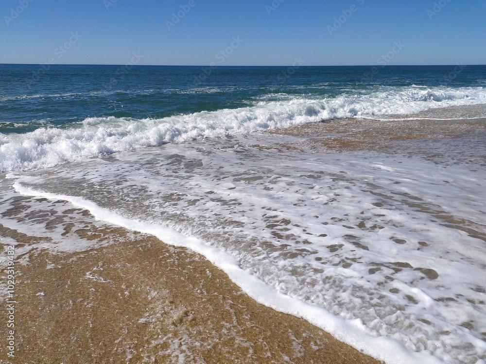 A serene beach at midday with gentle waves lapping the shore and clear blue skies inviting relaxation A serene beach at midday with gentle waves lapping the shore and clear blue skies inviting relaxation