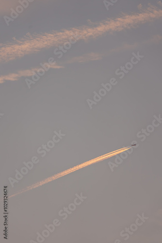 A plane flies through a clear sky, leaving a smoke trail behind