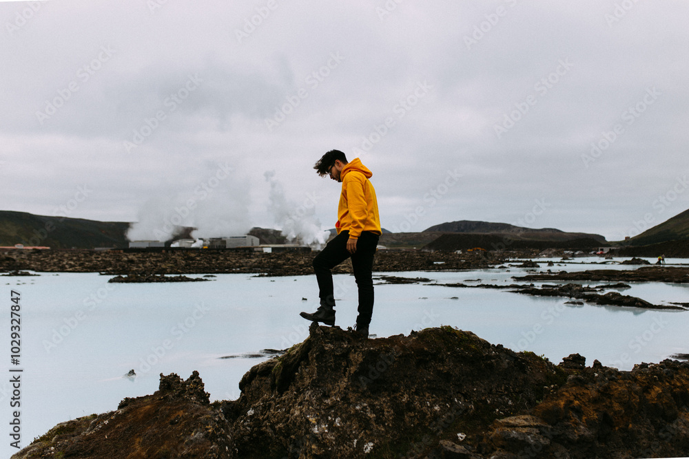 Obraz premium Person In Yellow Jacket Stands On Rugged Terrain By Water.