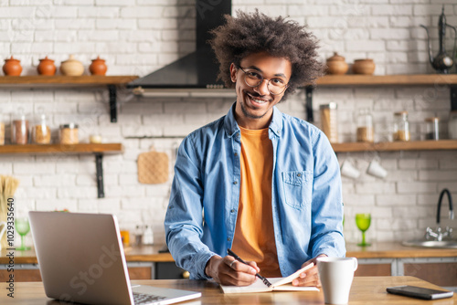 Portrait of young attrative African American man posing at modern loft kitchen interior with his laptop photo