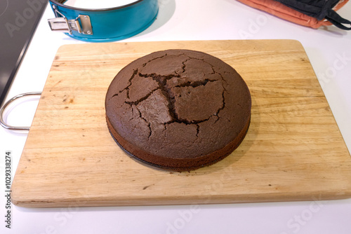 A freshly baked circle chocolate cake cracked placed on a wooden cutting board ready to be served photo