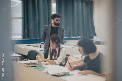 Wallpaper Mural Students are deeply engaged in studying at their desks in a classroom setting. A teacher stands by, overseeing their progress. This setting reflects a focused and collaborative educational environment Torontodigital.ca