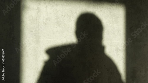 The man's shadow is cast on the wall. The scene is dark and brooding. The shadow of a man getting dressed and leaving.