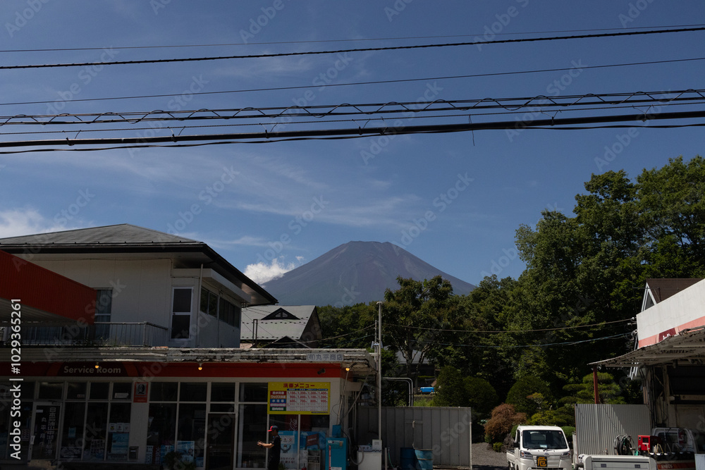This is a beautiful image of Mount Fuji stretching up into the clear blue sky. White clouds can be seen around the base being blocked. This was shot in Fujiyoshida Japan among the town. This is a beautiful image of Mount Fuji stretching up into the clear blue sky. White clouds can be seen around the base being blocked. This was shot in Fujiyoshida Japan among the town.