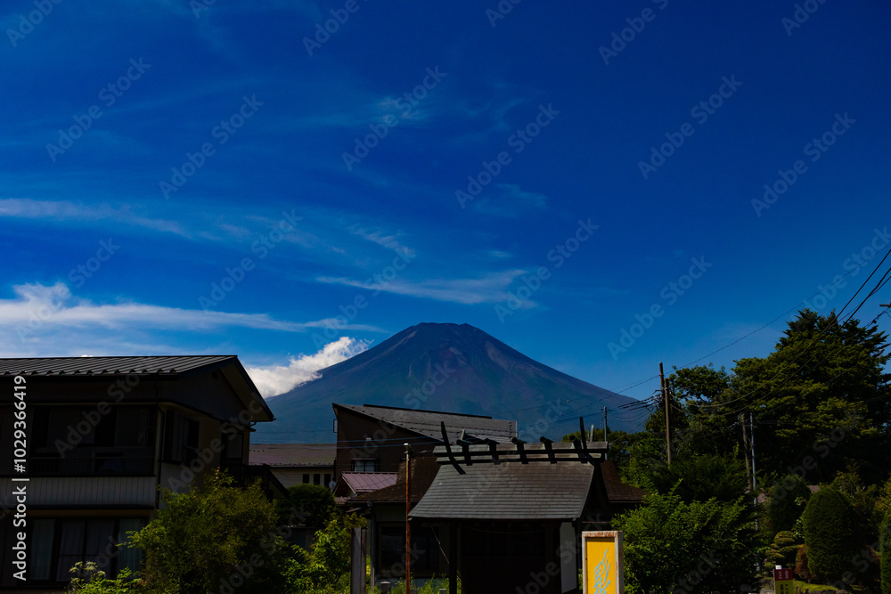 This is a beautiful image of Mount Fuji stretching up into the clear blue sky. White clouds can be seen around the base being blocked. This was shot in Fujiyoshida Japan among the town. This is a beautiful image of Mount Fuji stretching up into the clear blue sky. White clouds can be seen around the base being blocked. This was shot in Fujiyoshida Japan among the town.