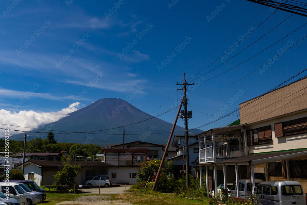 This is a beautiful image of Mount Fuji stretching up into the clear blue sky. White clouds can be seen around the base being blocked. This was shot in Fujiyoshida Japan among the town. This is a beautiful image of Mount Fuji stretching up into the clear blue sky. White clouds can be seen around the base being blocked. This was shot in Fujiyoshida Japan among the town.