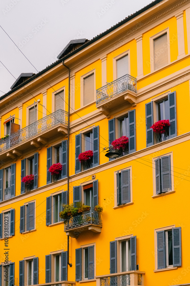 facade of the Italian yellow apartment building with pink flowers on the windows facade of the Italian yellow apartment building with pink flowers on the windows